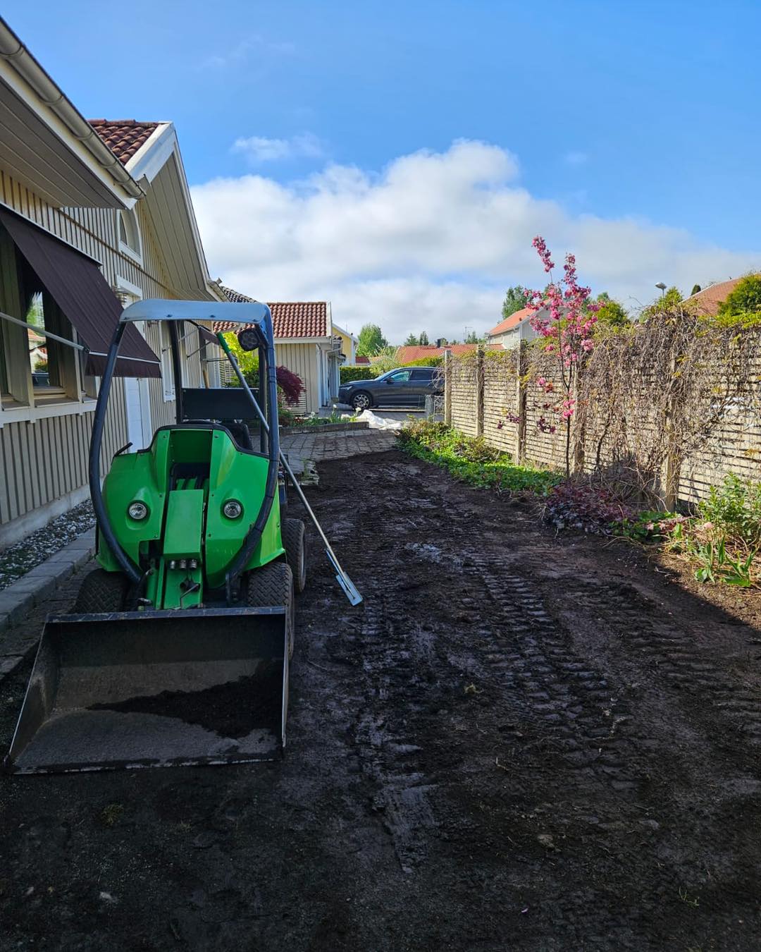 Liten lastmaskin på nyplanerad jordyta intill ett radhus.
