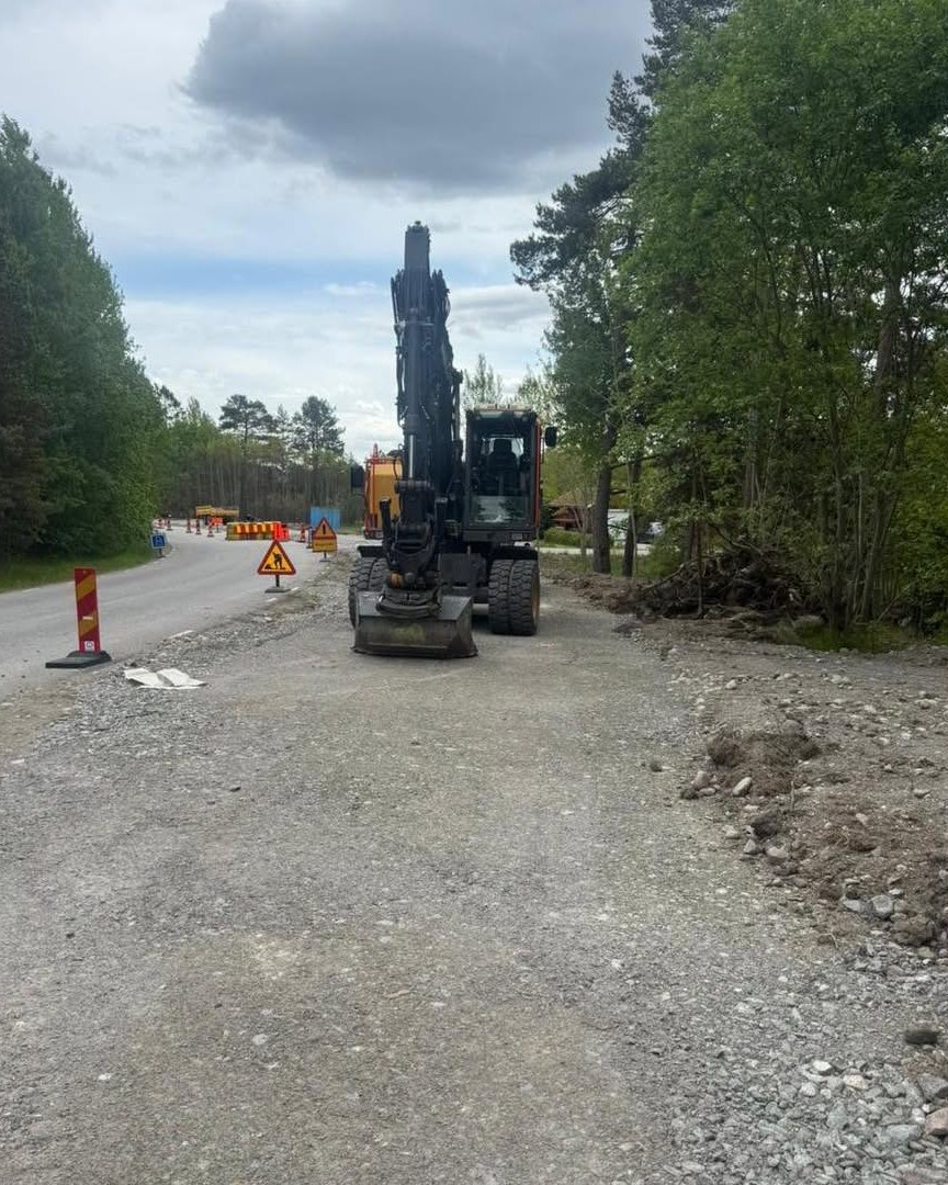 Hjulgrävare med skopan på marken vid ett pågående anläggningsarbete längs en väg.