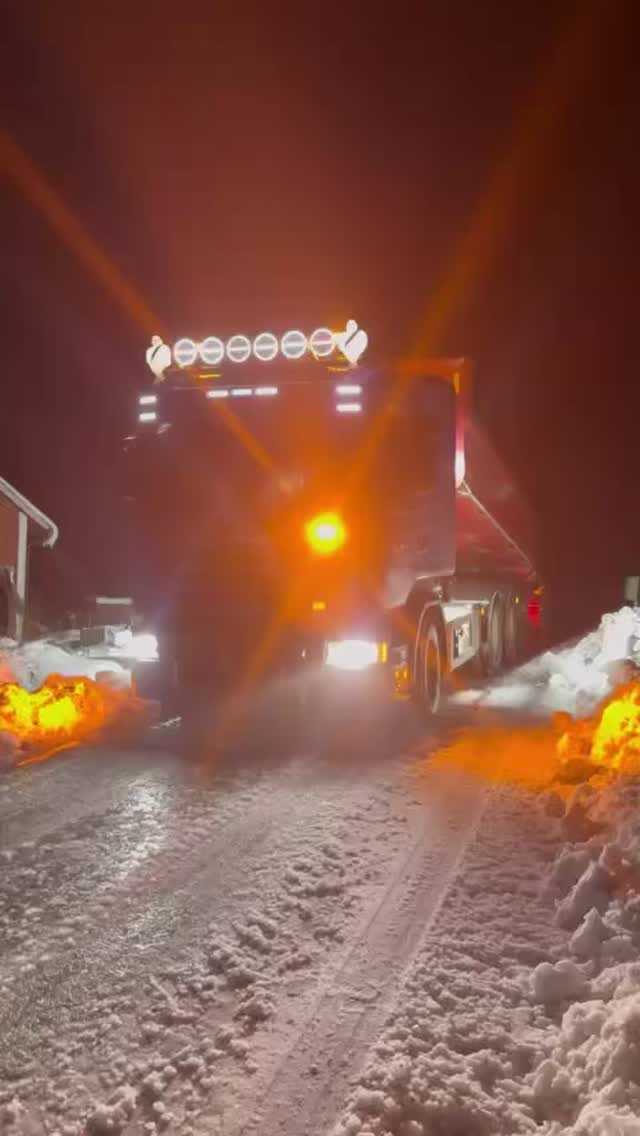 Lastbil med arbetsbelysning röjer snö en vinterkväll.