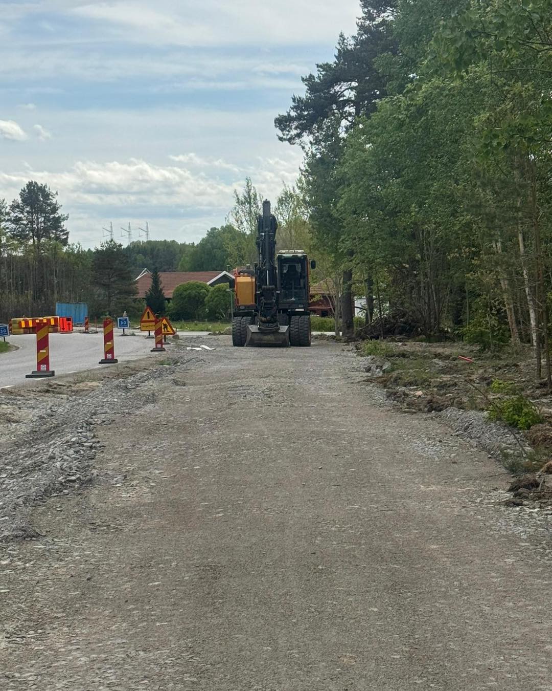 Grävmaskin bygger ny gång- och cykelbana längs en väg, med avspärrningar.