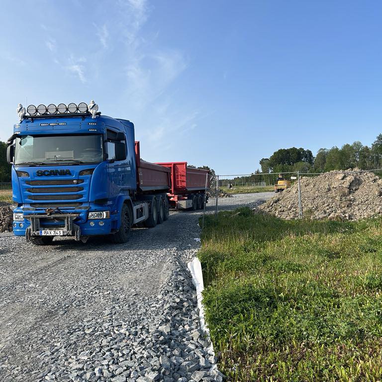 Blå Scania-tippbil vid en nyanlagd grusyta.