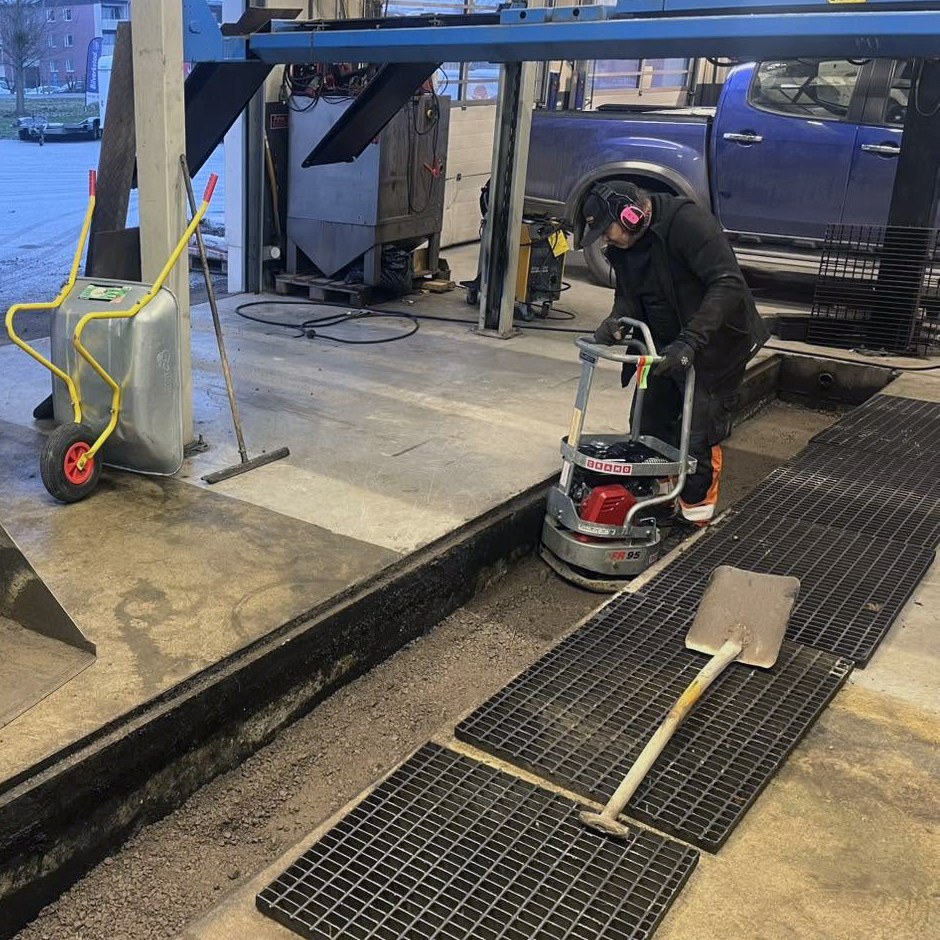 Arbetare med vibratorplatta i ett verkstadsgolv.