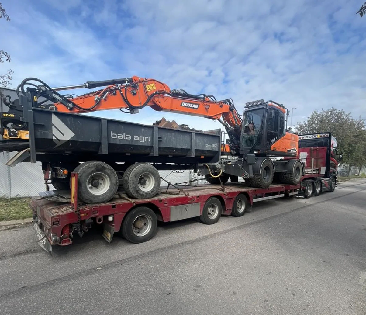 Lastbil med maskintrailer lastad med grävmaskin och dumperkärra
